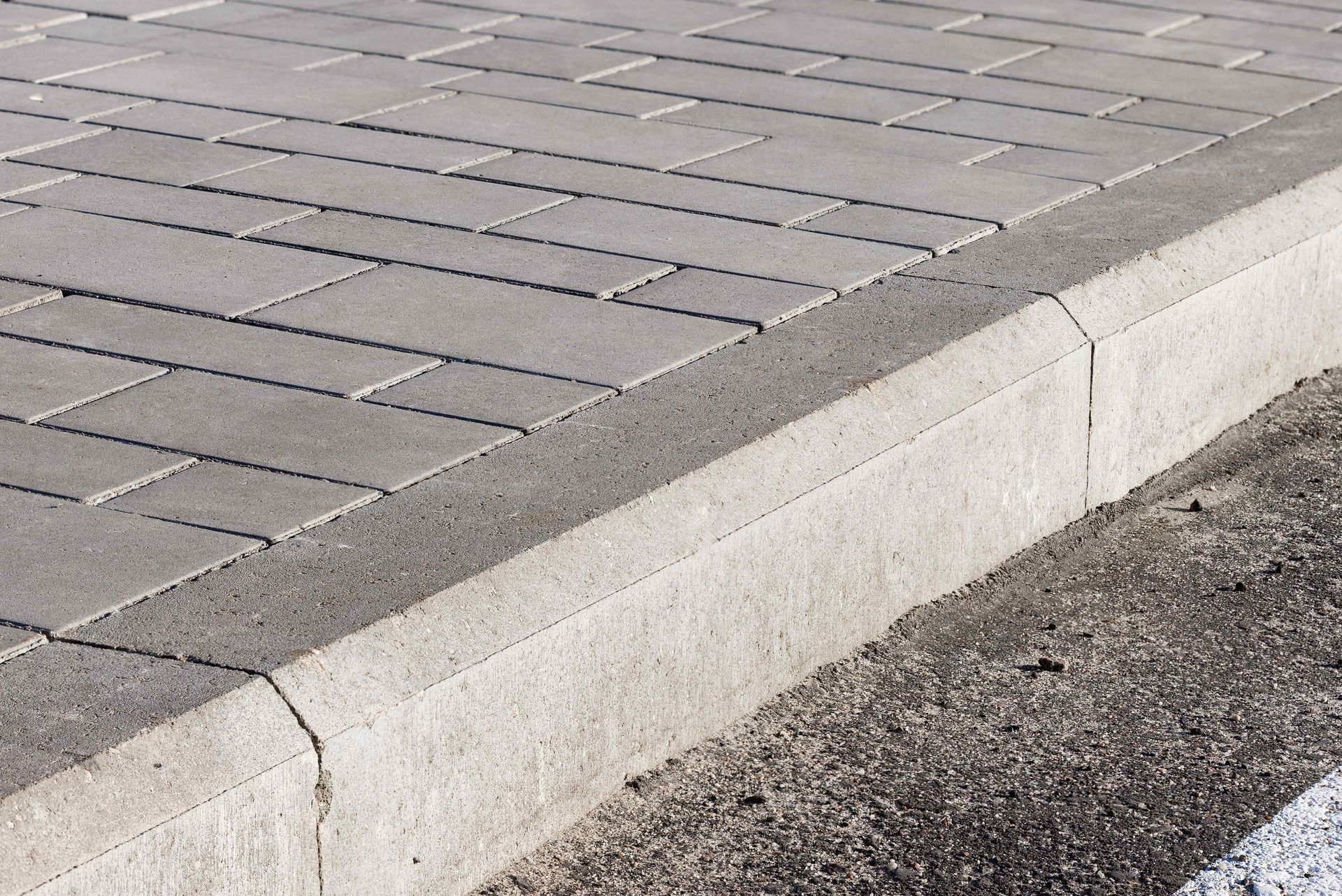 A low concrete curb bordering gray paver tiles and dark asphalt road.