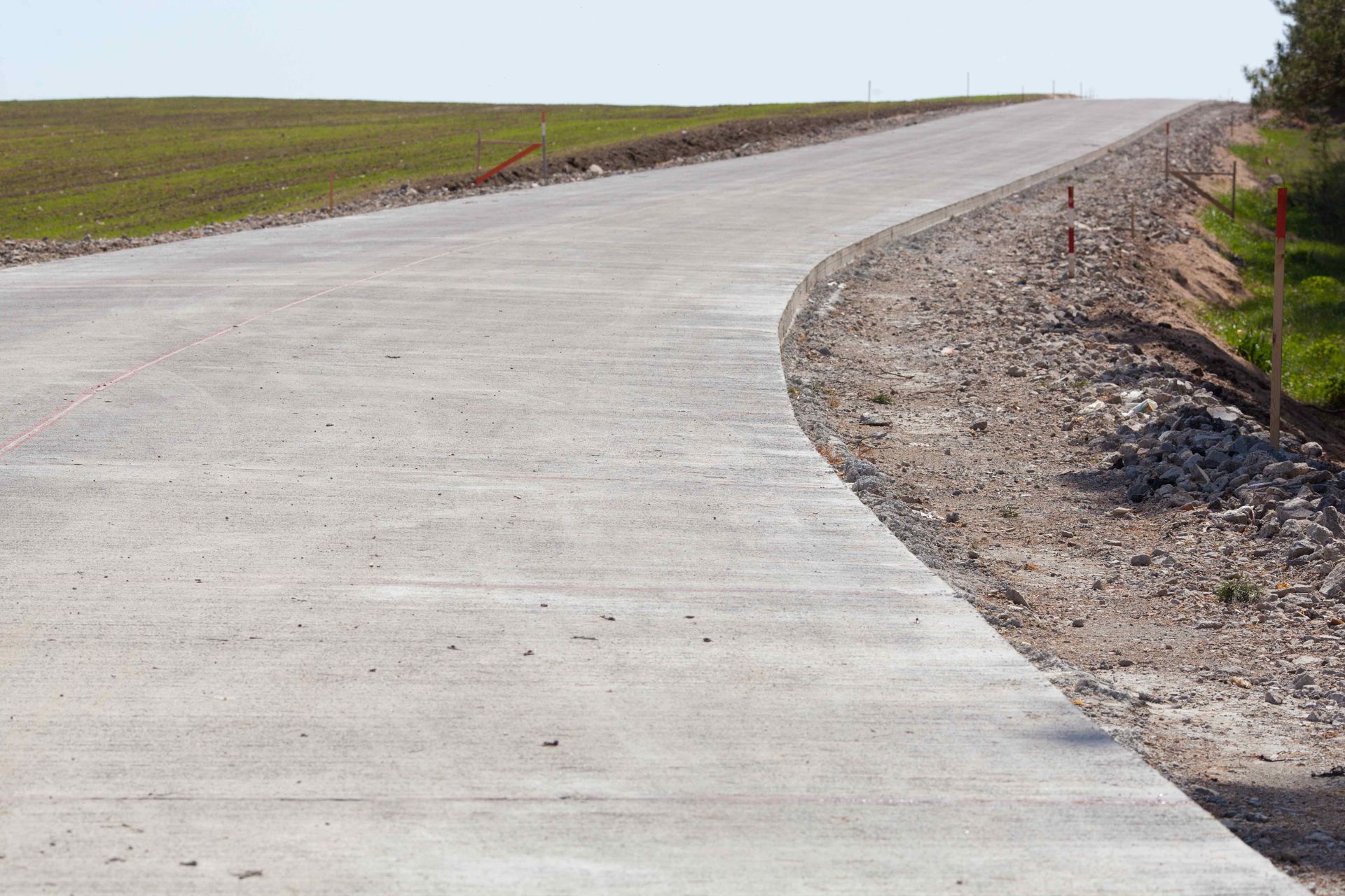 A concrete road winds upward through a grassy, hilly landscape under a clear sky.