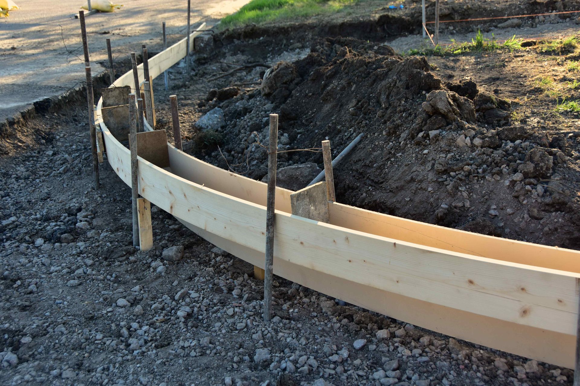 Wooden concrete forms set up in a curve along a gravel and dirt construction site.