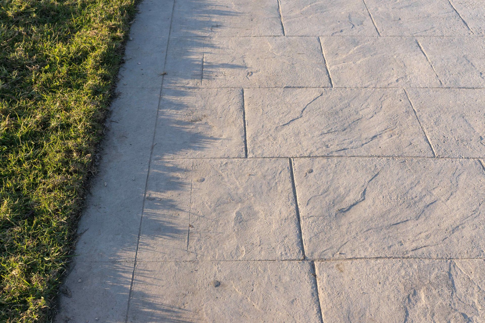 A paved walkway made of rectangular stone tiles next to a strip of green grass.