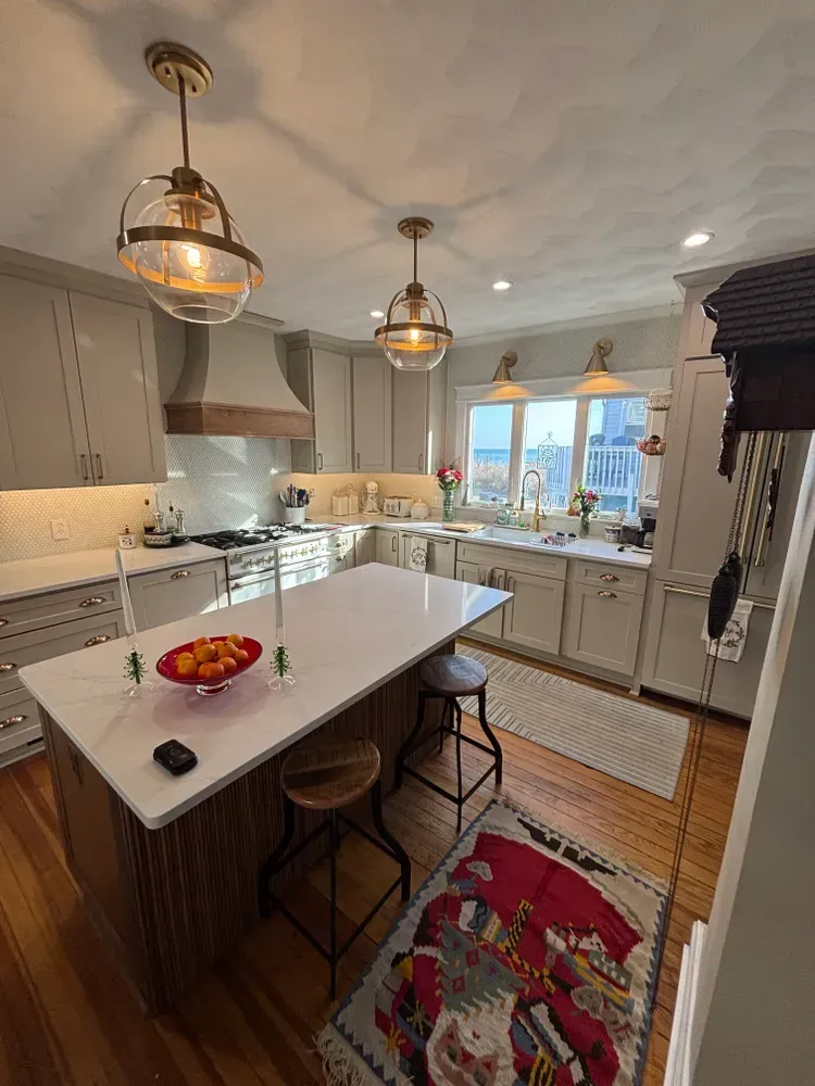 Bright kitchen with white cabinets, large island, pendant lights, and a red runner rug