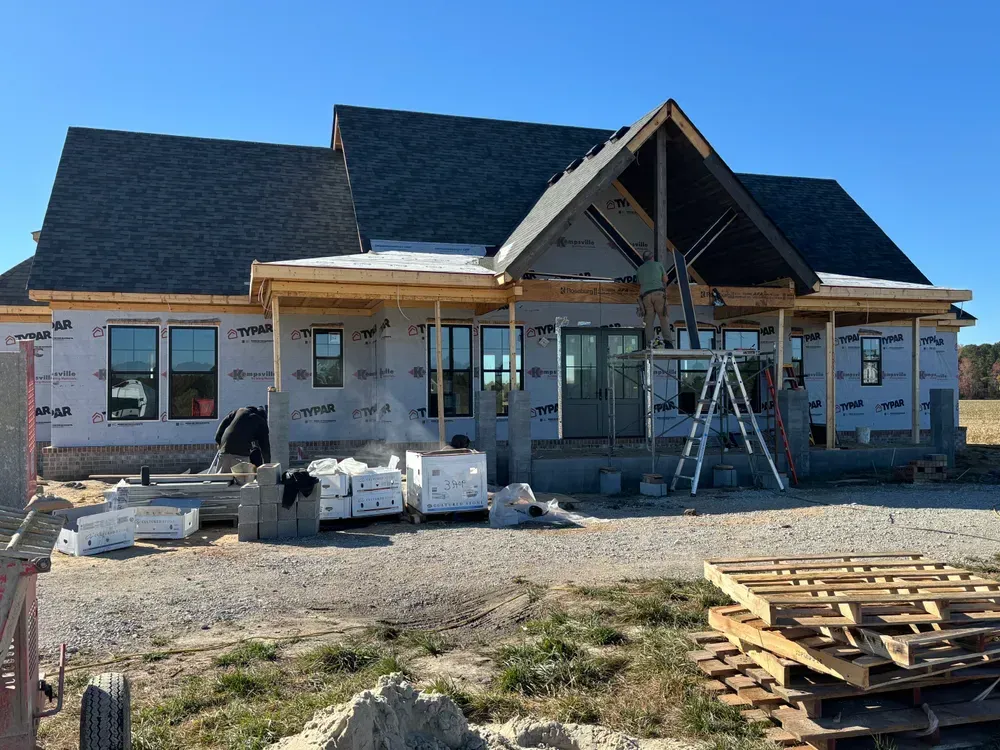 House under construction with scaffolding, exposed framing, and building materials in front.