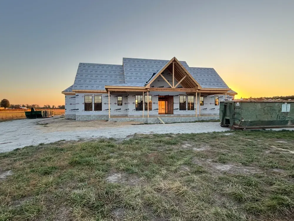 New house under construction at sunset, with a green dumpster in the foreground.