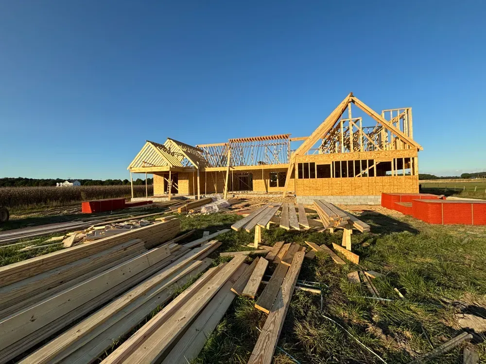 Wood-framed house under construction with lumber stacks in the foreground at sunset
