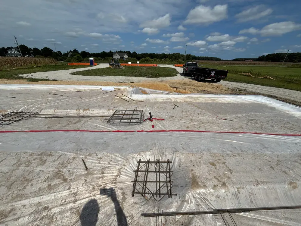 Construction site with white concrete slab, exposed rebar, and a pickup truck under a cloudy sky