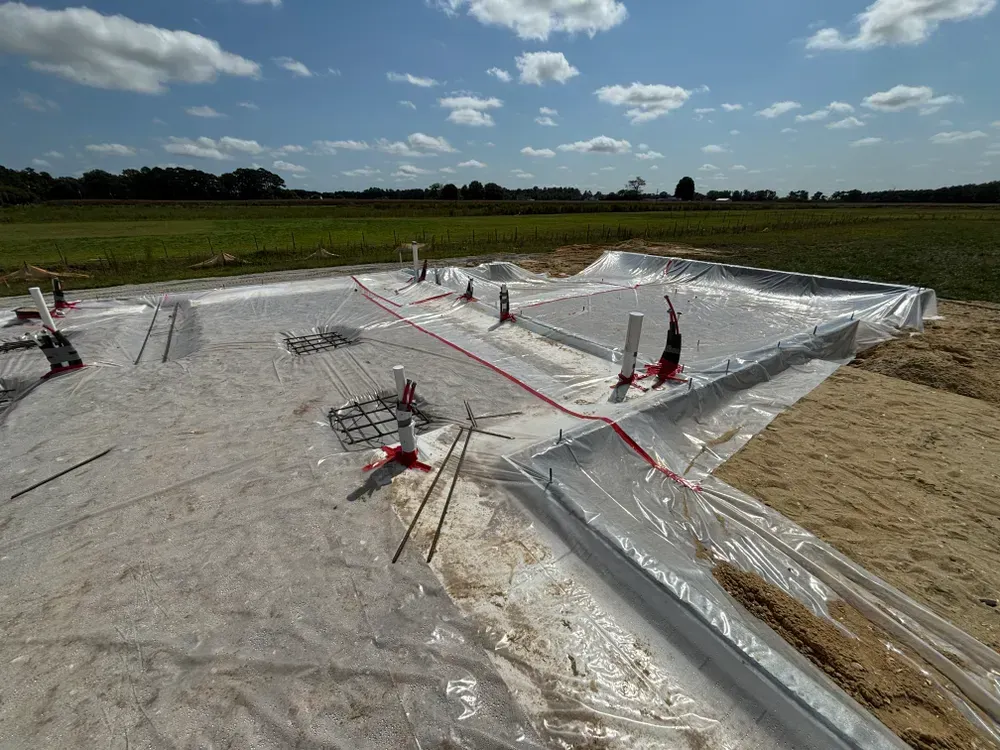 Solar panel installation with silver reflective sheets and red cables on a grassy field under a cloudy sky