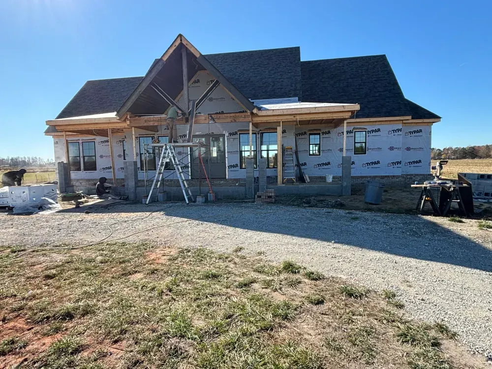 Partially built house with front porch and ladders on a gravel lot under a clear sky