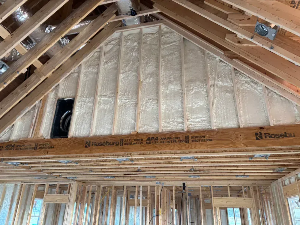 Unfinished attic framing with exposed wooden rafters and insulated gable wall under construction