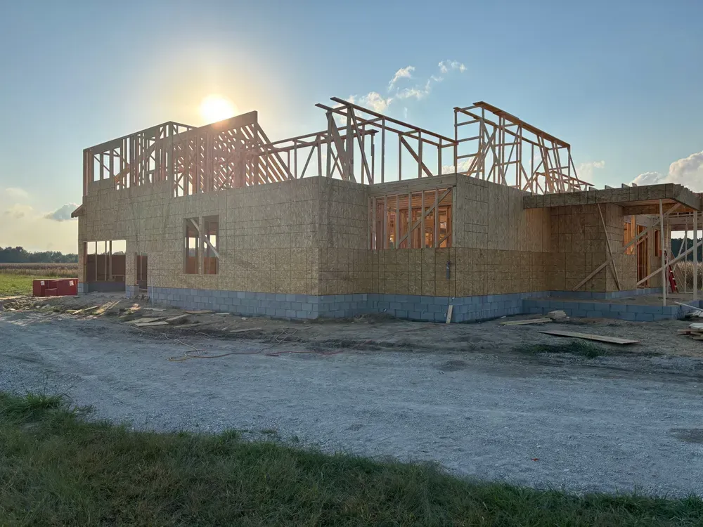 Partially built house with exposed wooden framing at sunset on a gravel lot