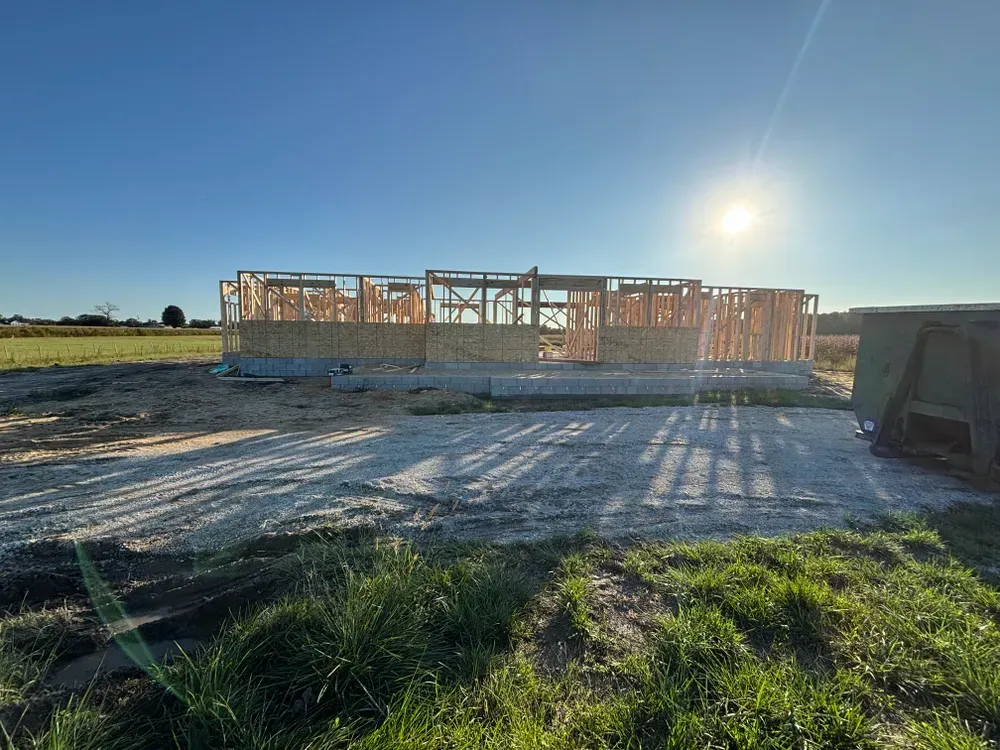 Wood-framed house under construction on a sunny open lot with long shadows.