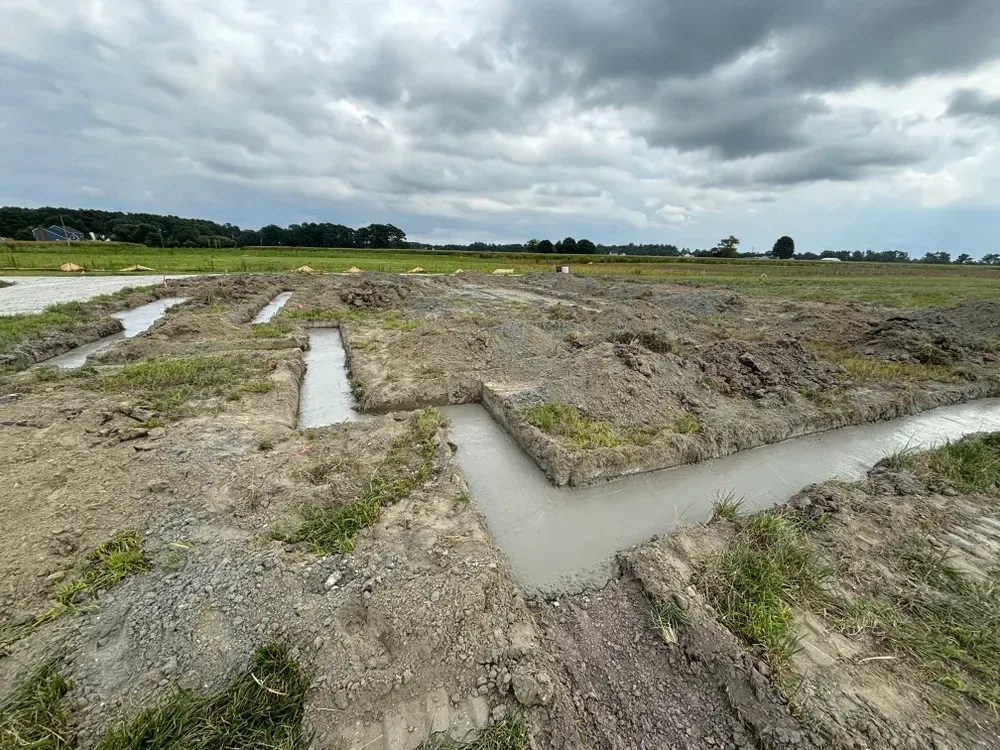 Flooded dirt field with narrow muddy trenches under a cloudy sky.