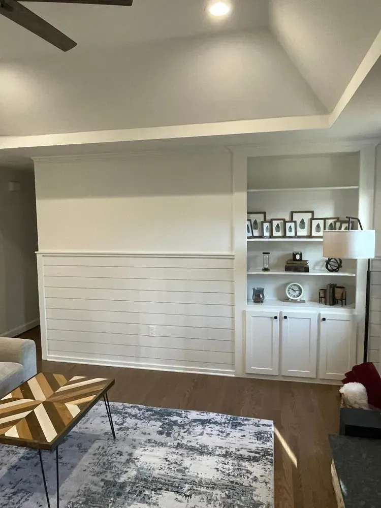 Bright living room with a white built-in cabinet, framed photos, and a patterned rug under recessed lights