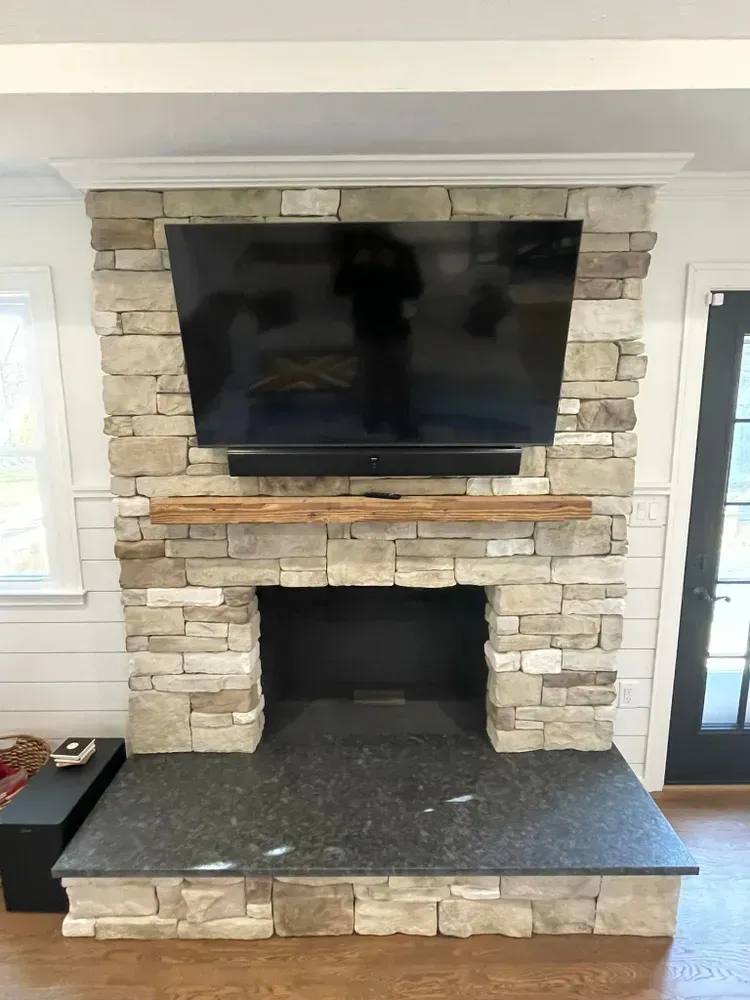 Stone fireplace with a flat-screen TV mounted above a black hearth opening and dark stone ledge.