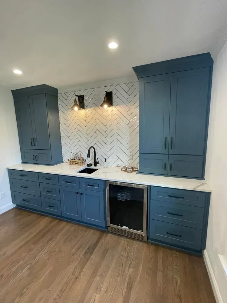 Modern kitchen with blue cabinets, white countertops, herringbone backsplash, and wood floors