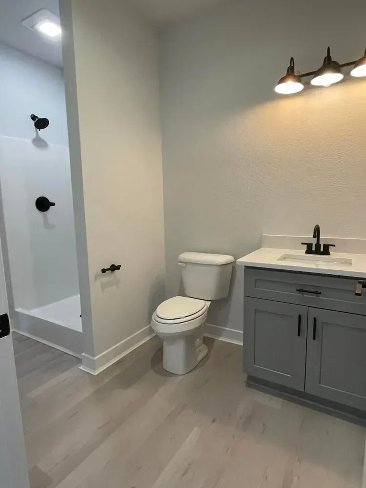 Modern bathroom with shower, toilet, and gray vanity with sink and lights.
