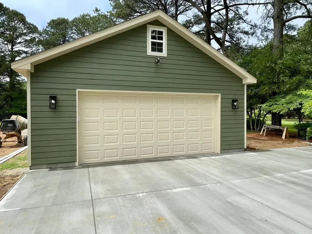 Green detached garage with beige door and concrete driveway