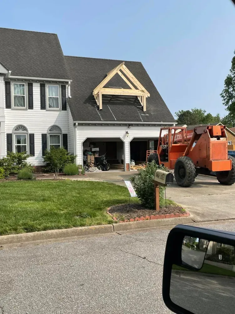 Orange tractor near a white house under roof repair on a suburban street