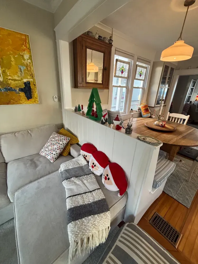 Cozy living room with gray sofa, holiday decor, and wooden dining table by a bright window.