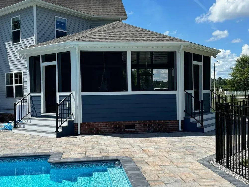 Screened porch with dark blue siding beside a backyard pool and patio, next to a house