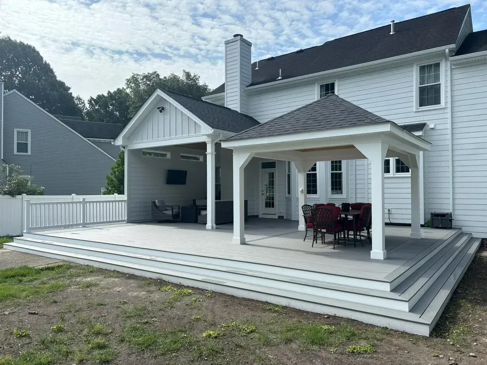 White house backyard with a large multi-level deck, covered patio, and outdoor seating under a cloudy sky