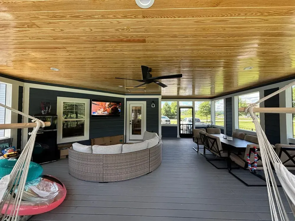 Covered porch with a curved bar, TV, ceiling fan, chairs, and hammocks overlooking a yard and water.