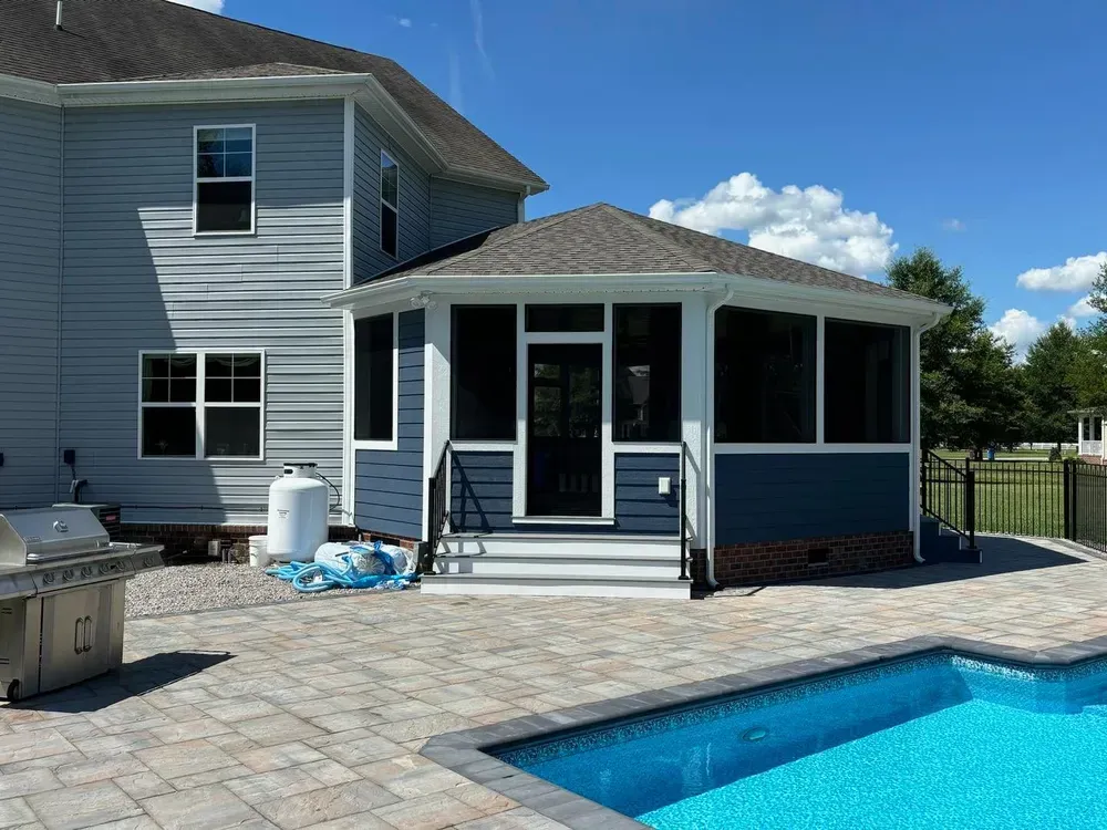 Backyard pool beside a two-story house with a screened porch and patio pavers