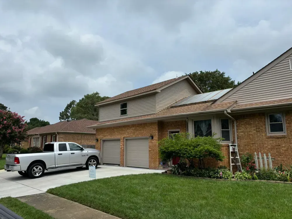 Suburban brick house with two garages, white pickup in driveway, and green lawn under cloudy sky