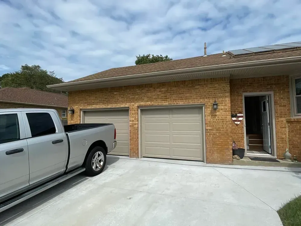 Single-story brick house with white garage door, driveway, parked pickup truck, and open front door