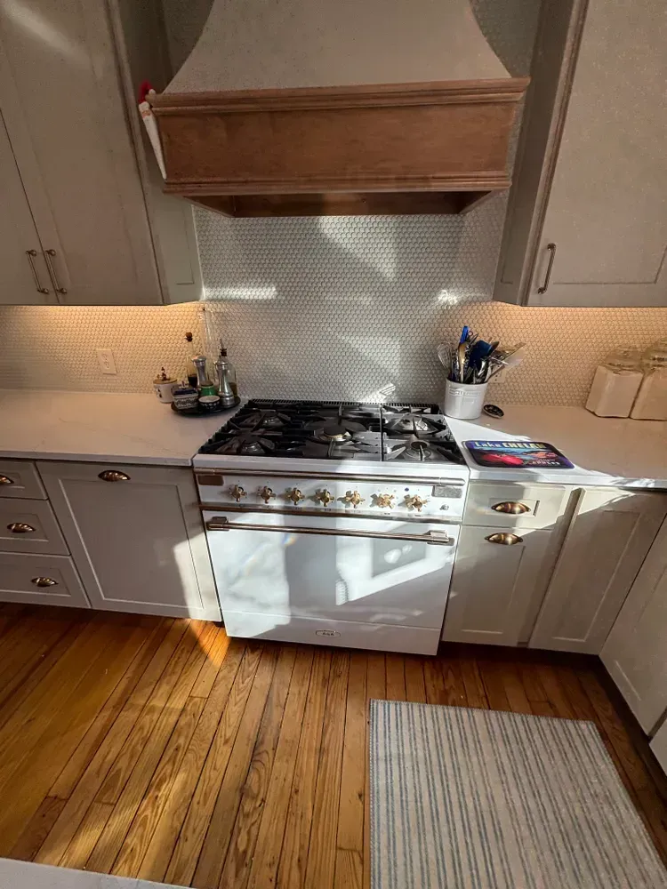 Bright kitchen with white cabinets, gas stove, wood hood, and sunlight on the floor.