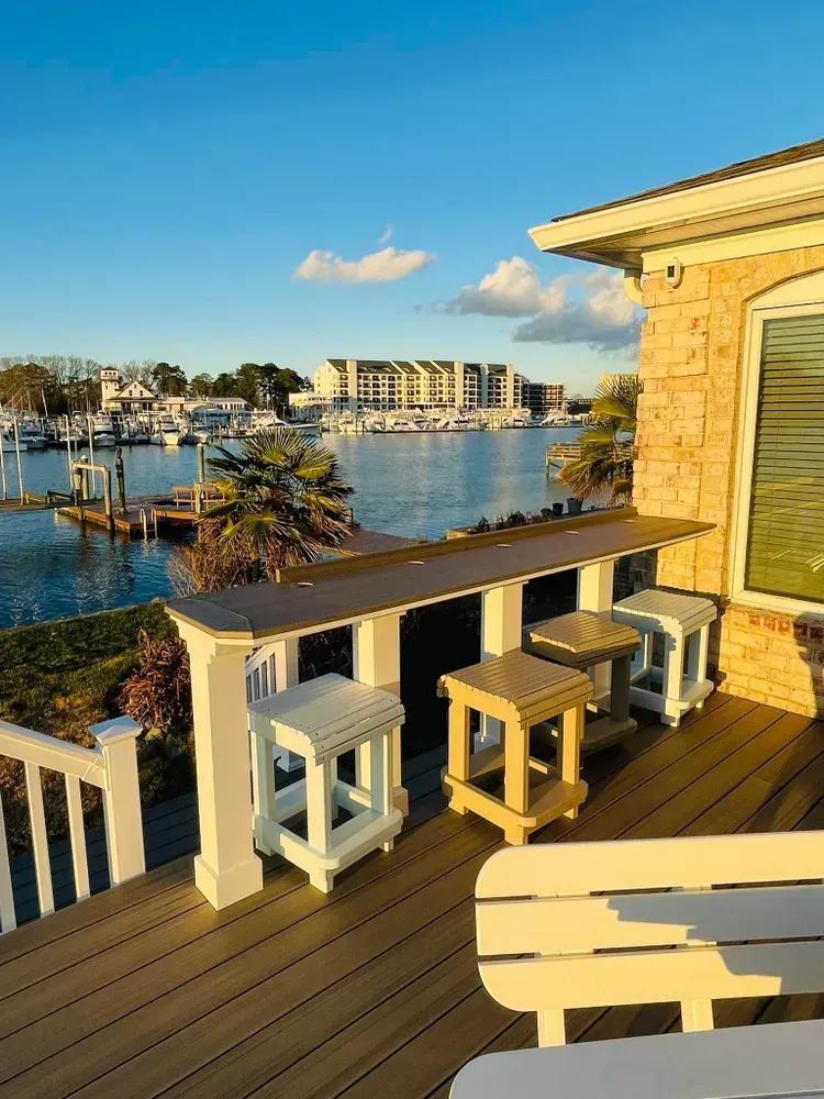 Sunny marina-view deck with white stools and a bar overlooking water and boats
