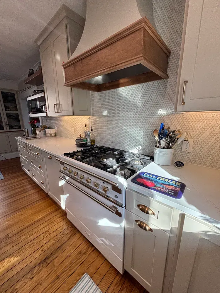 Modern kitchen with white cabinets, wood range hood, gas stove, and tiled backsplash