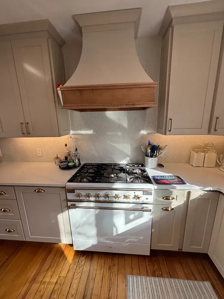 White kitchen with cabinets, gas range, and decorative hood over a tiled backsplash and wood floor.