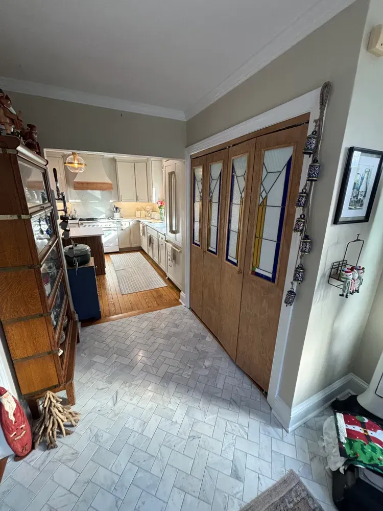 Hallway with wooden double doors, patterned tile floor, and a view into a bright kitchen ahead