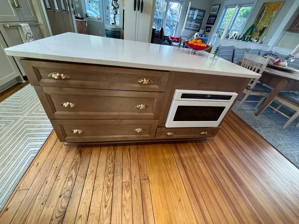 Wooden kitchen island with white countertop, drawers, and built-in oven in a bright dining area
