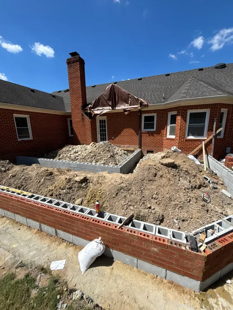 Brick courtyard under renovation with dirt pile, partially rebuilt walls, and a chimney against a blue sky