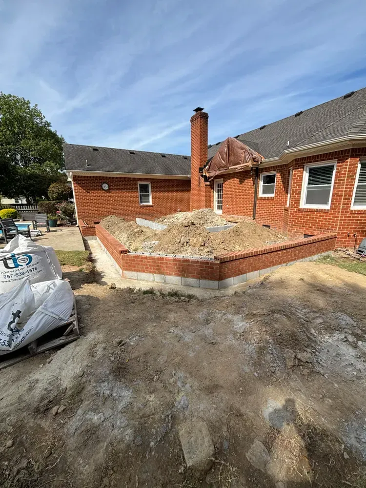 Backyard construction site with red brick house, raised brick planter, dirt piles, and a chimney