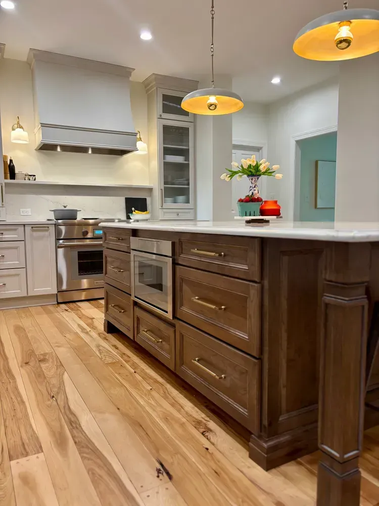 Modern kitchen with a large island, wood floors, pendant lights, and stainless steel appliances.
