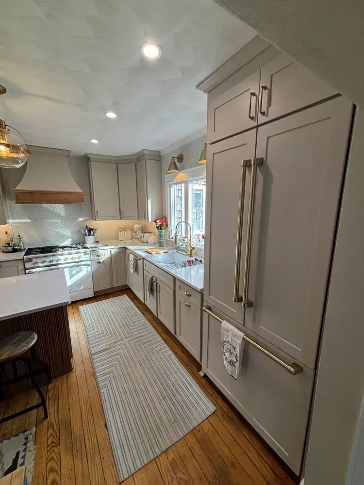 Modern galley kitchen with gray cabinets, white counters, stainless appliances, and a window over the sink