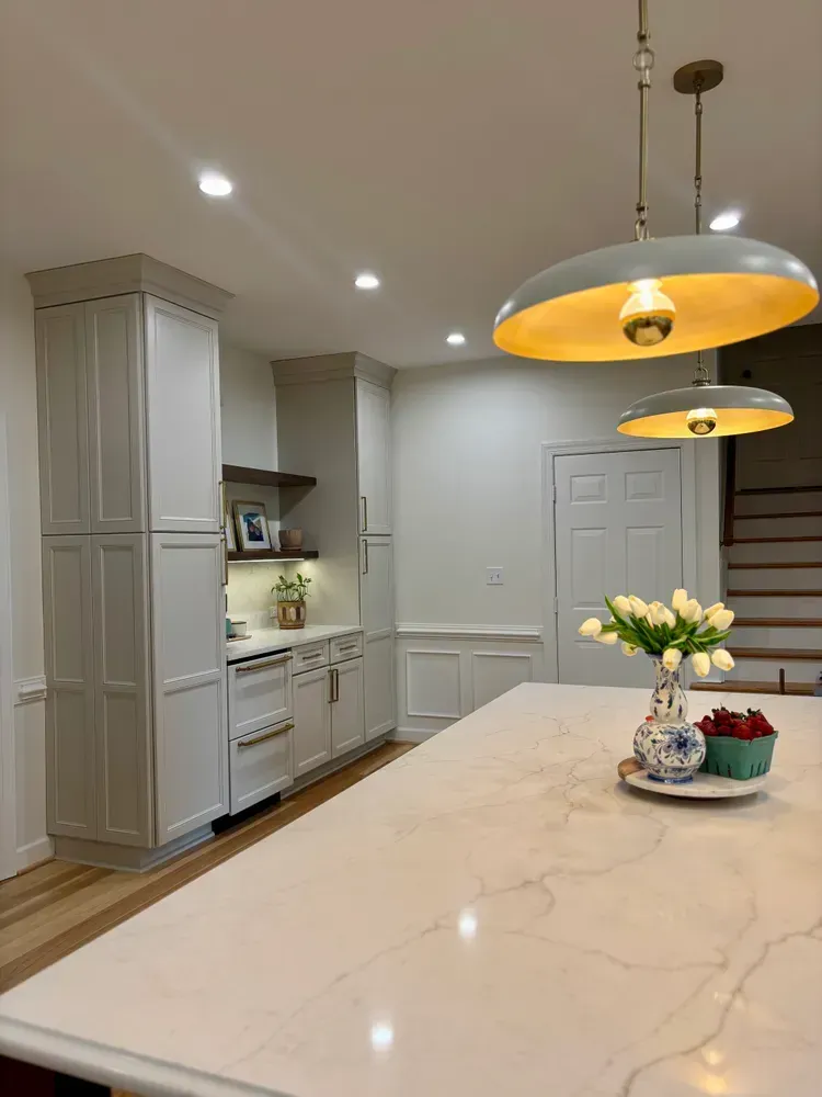 Modern white kitchen with marble island, pendant lights, and vase of flowers