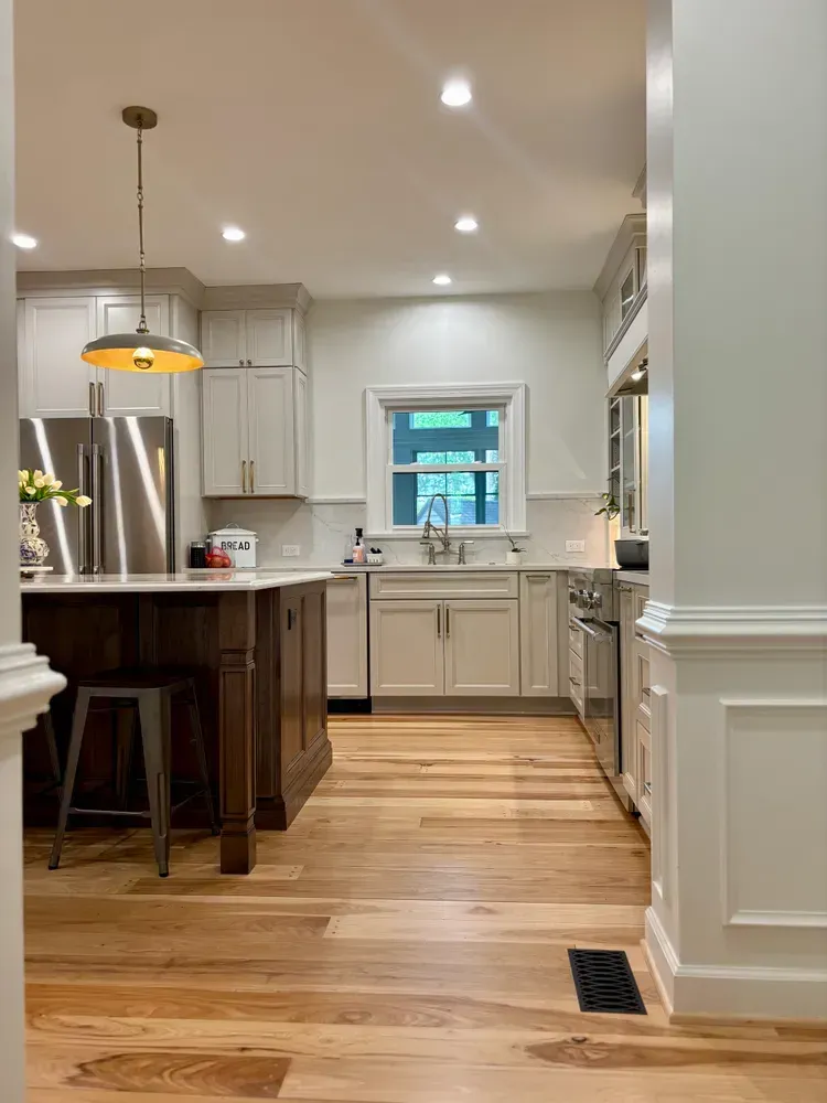 Bright kitchen with white cabinets, wood floor, island, and stainless steel fridge under recessed lights.