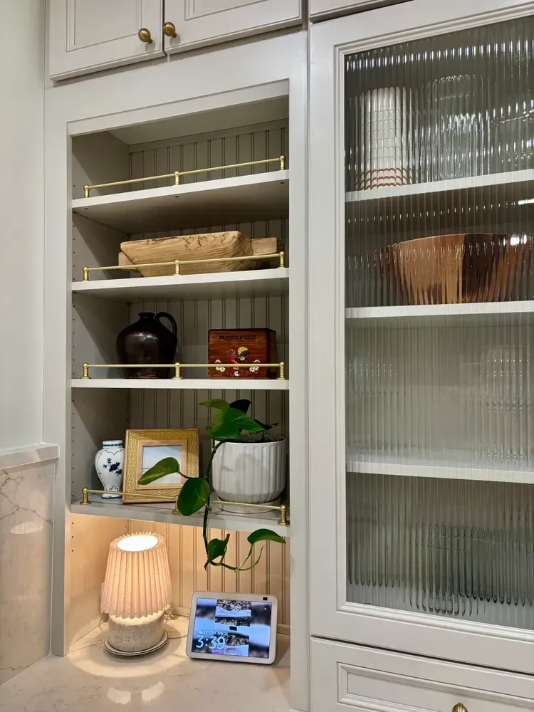 Built-in kitchen cabinets with shelves, decor, lamp, plant, and a tablet near a window.
