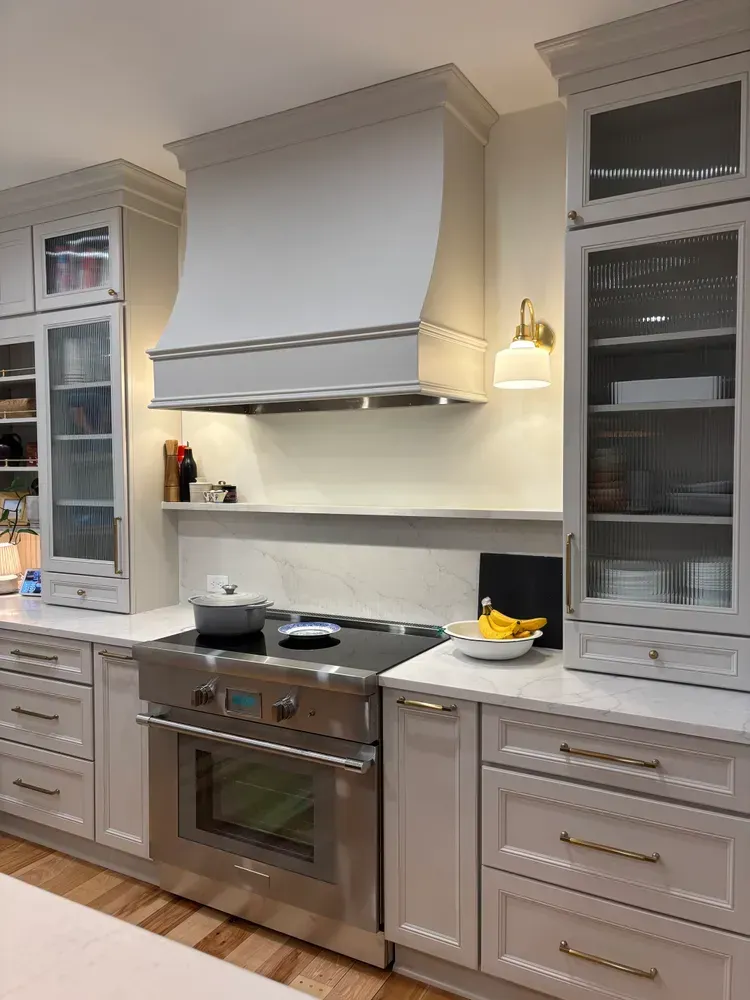 Modern white kitchen with stainless steel range, glass cabinets, and beige countertops