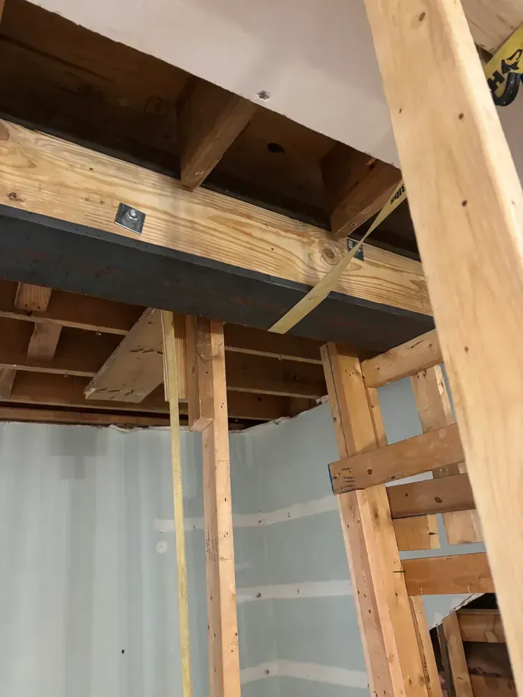 Partially gutted room with exposed wooden beams, studs, and a ladder or support post, viewed from below