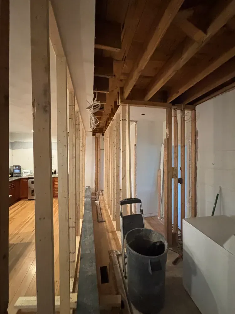 Renovation in progress: unfinished basement with exposed studs, beams, and a large pipe in the foreground
