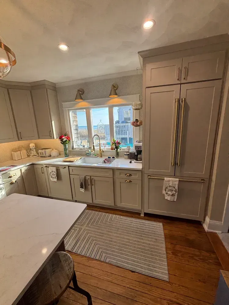Bright kitchen with gray cabinets, white island, farmhouse sink, and a window over the countertop.