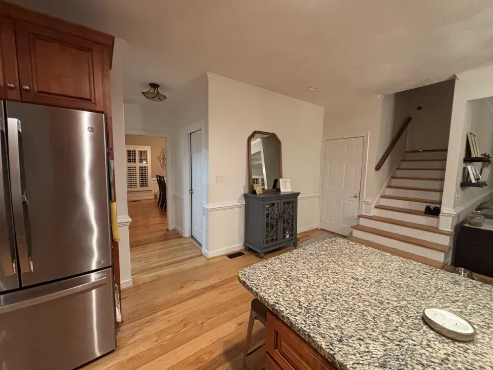 Modern kitchen with stainless fridge, island, wood floors, and staircase in the background