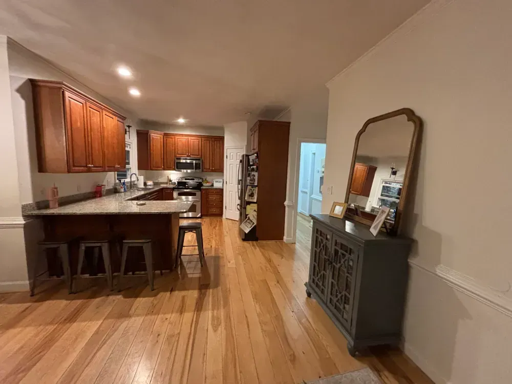 Open kitchen and dining area with wood floors, island stools, and a gray sideboard with mirror.