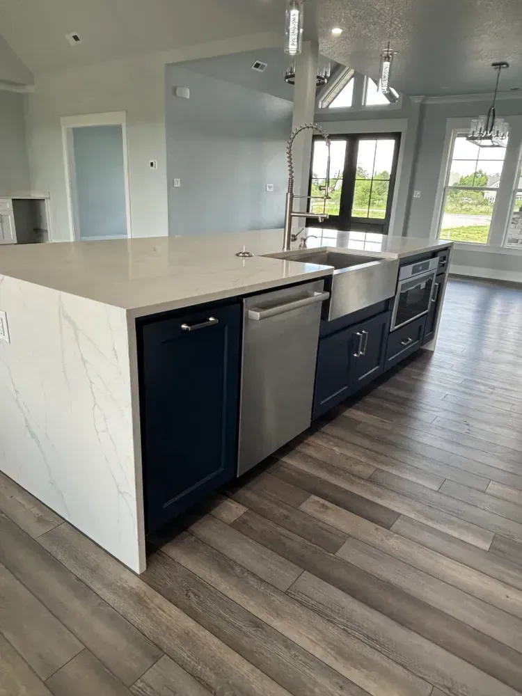 Modern kitchen with white island, black cabinets, stainless dishwasher, and wood-look flooring