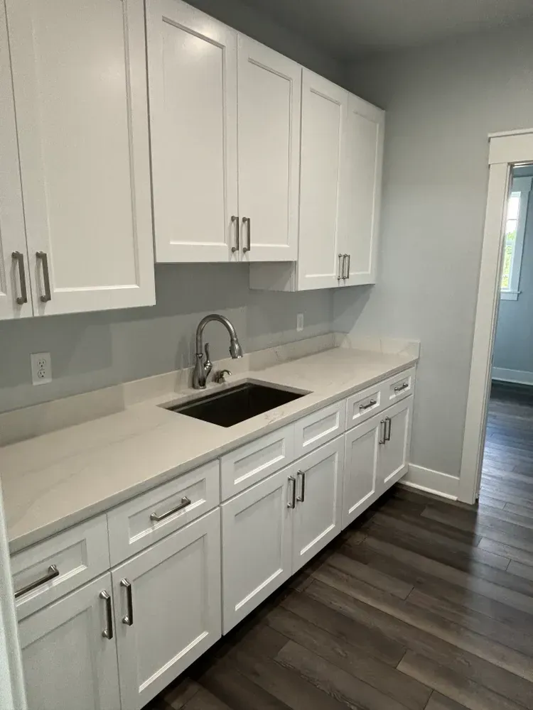 White kitchen with modern cabinets, light countertops, black sink, and dark wood flooring