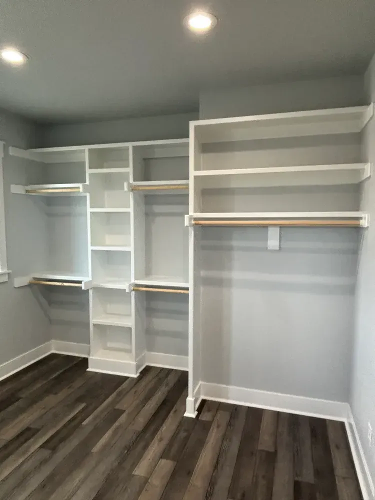 White walk-in closet with built-in shelves, hanging rods, and dark wood flooring under recessed lighting